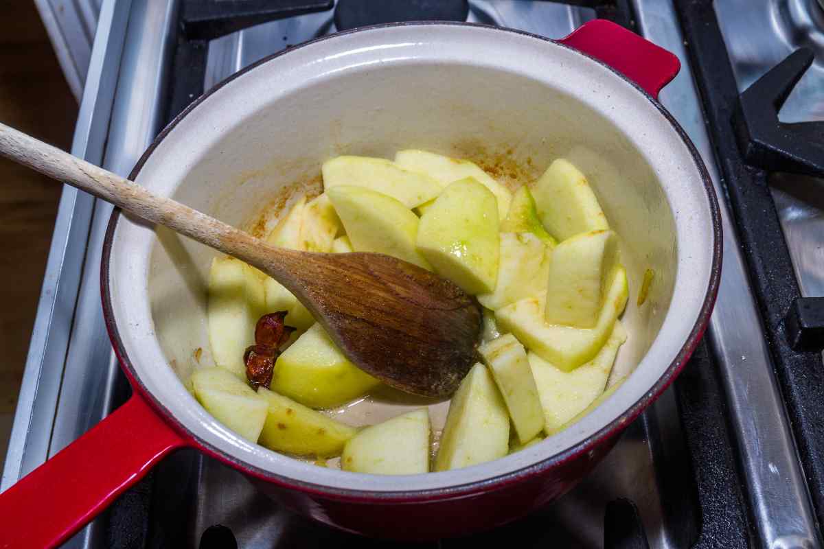 Image of a spoon stirring some peeled sliced apples in a pan to soften them, this is part of a blog about making apple crumble with kids