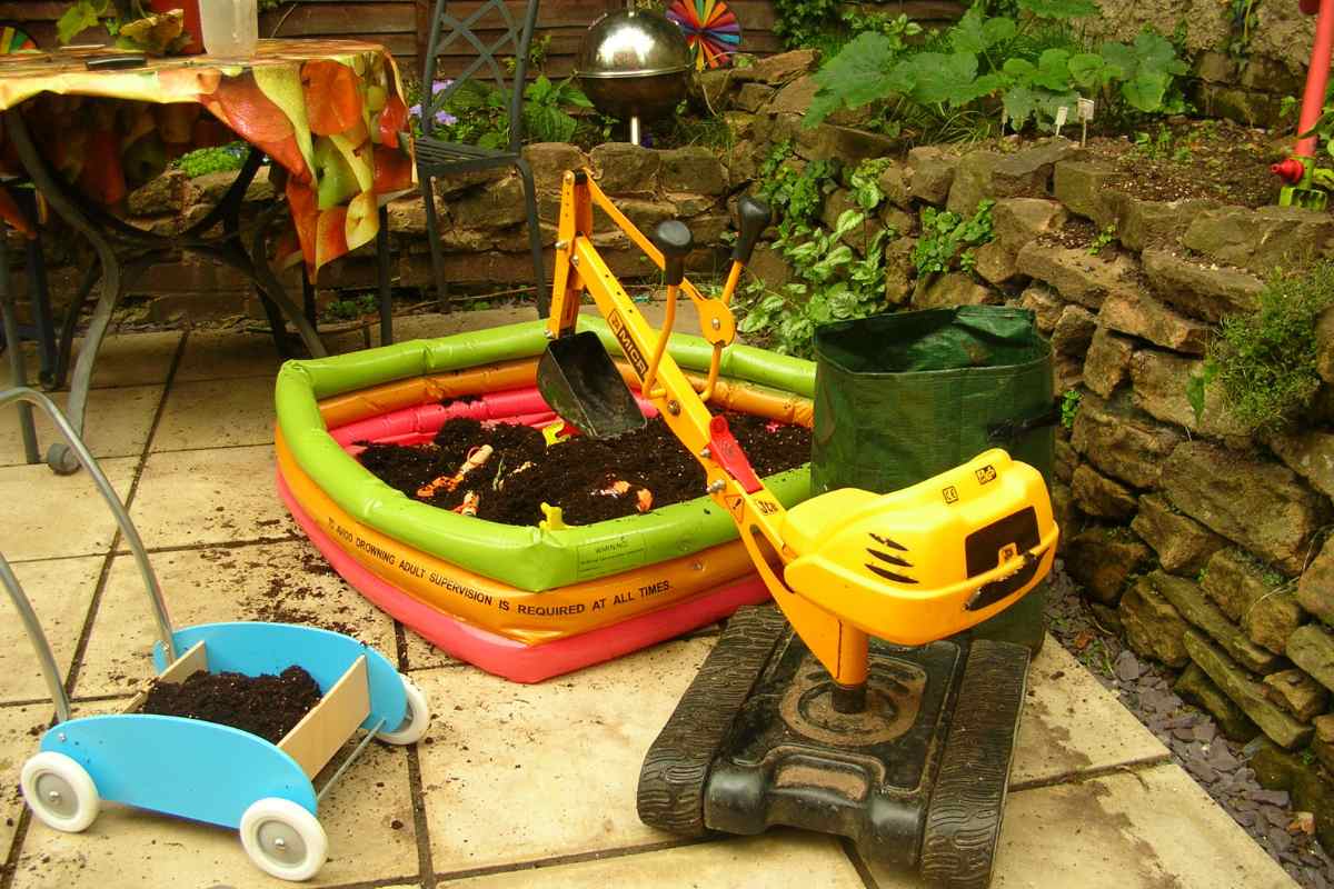 Image of outdoor construction toys - a digger and some tractor toys – and a paddling pool half filled with soil, as part of a blog about harvesting potatoes with children