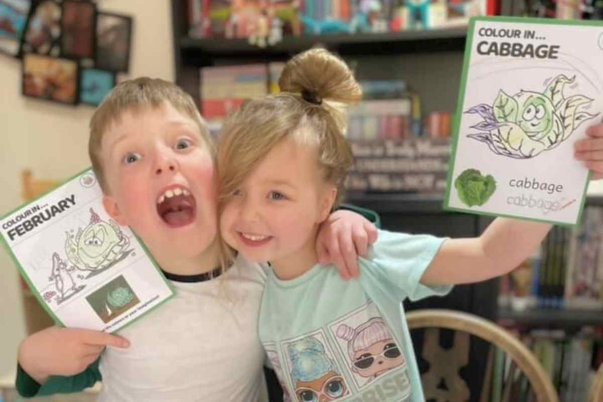 Image of two children who are Little Foodies Club members, they are holding their veggie related colouring in the air and laughing.