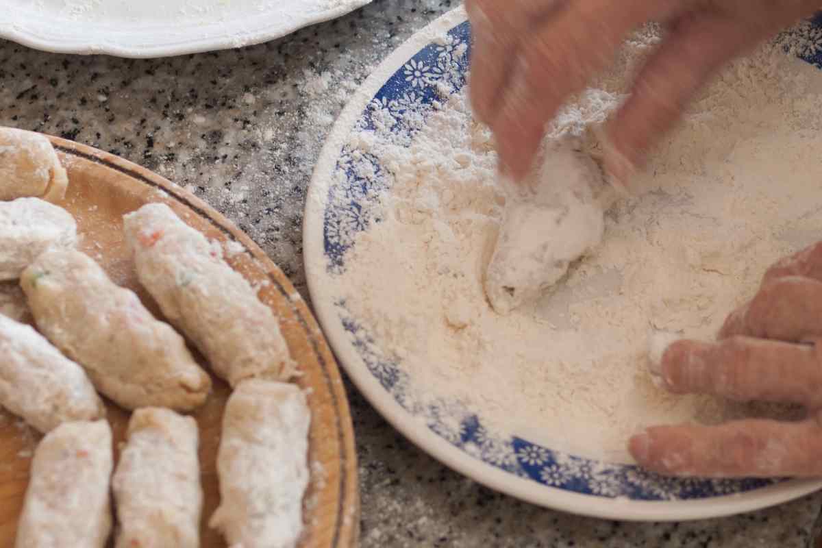 Image of a hand rolling clumps of mashed parsnips into sausage shapes and rolling them in a plate of flour, as part of a blog about making a parsnip croquettes recipe with kids