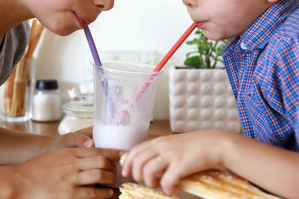 Image of two children’s chins showing they are drinking from a milkshake in the middle with straws, this is part of a blog about making pear and coconut milkshake with kids