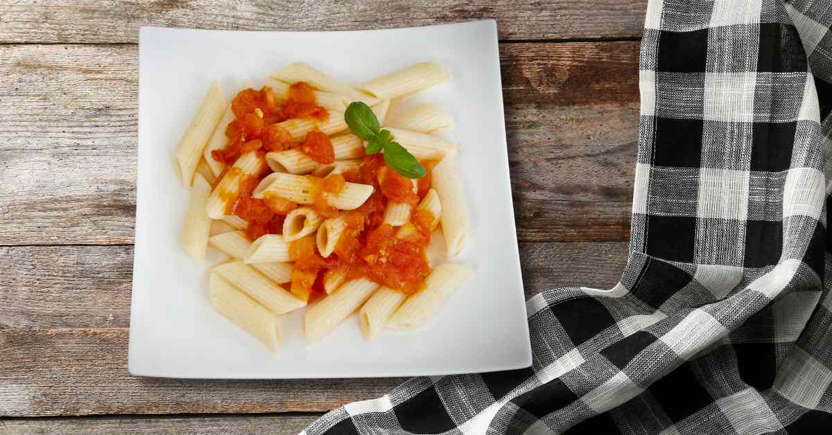 Image of some penne pasta on a plate, with squished tomatoes on top as a simple sauce as part of a blog about making squished tomato pasta with kids
