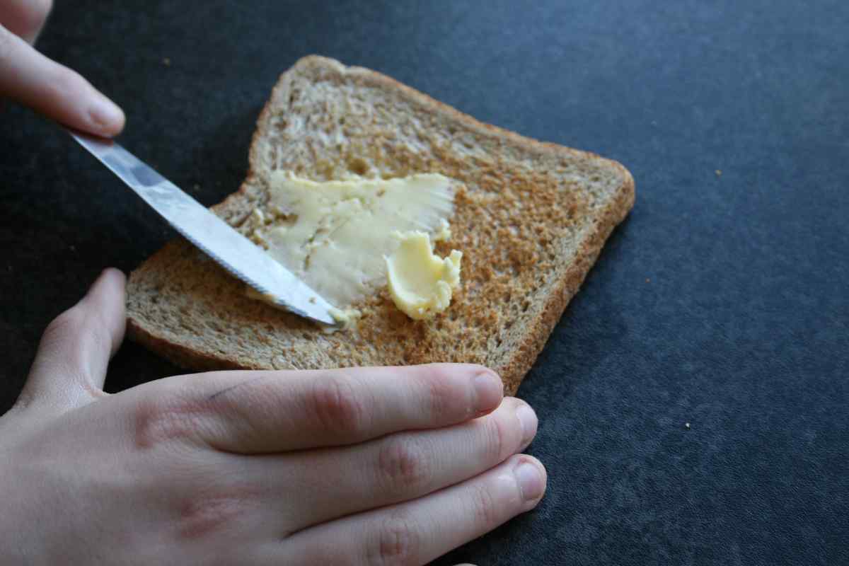 Picture of a child's hand spreading butter onto toast, as part of a blog about a Valentine's recipe for kids to make independently called Love Toast.