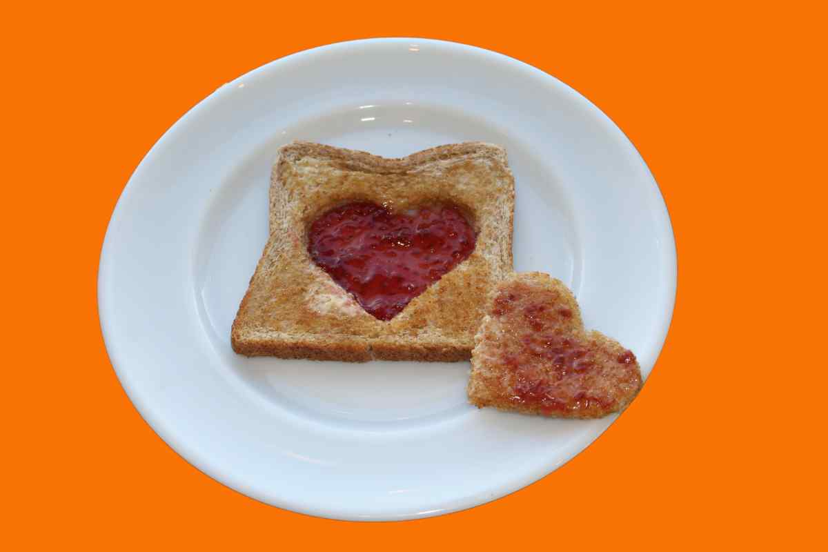 A white plate with toast on it, a heart shaped cut out taken out of the middle and put on one side, the toast heart is spread with jam and the cut out from the toast has jam filling it, this is the finished image for our guide on how to make Valentine's Love Toast with kids.