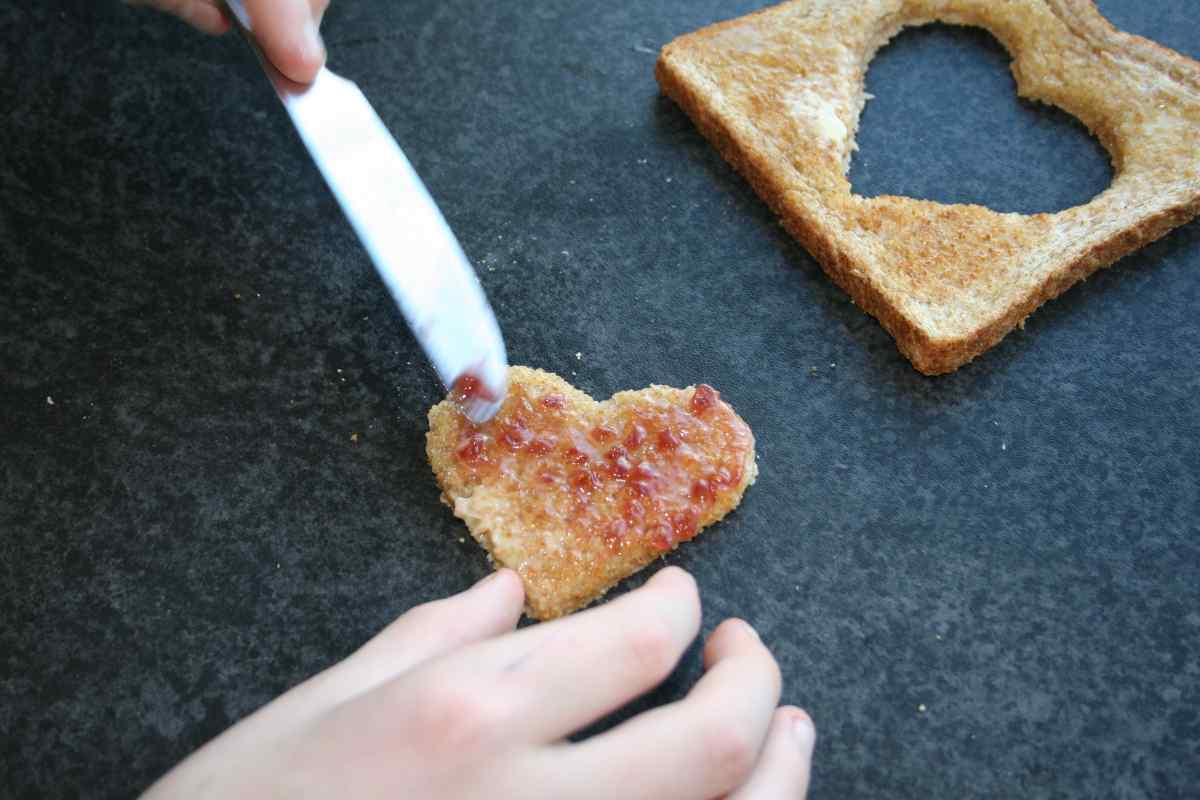 Picture of a child's hands spreading jam onto a small heart shaped piece of toast, as part of a blog about a Valentine's recipe for kids to make independently called Love Toast.