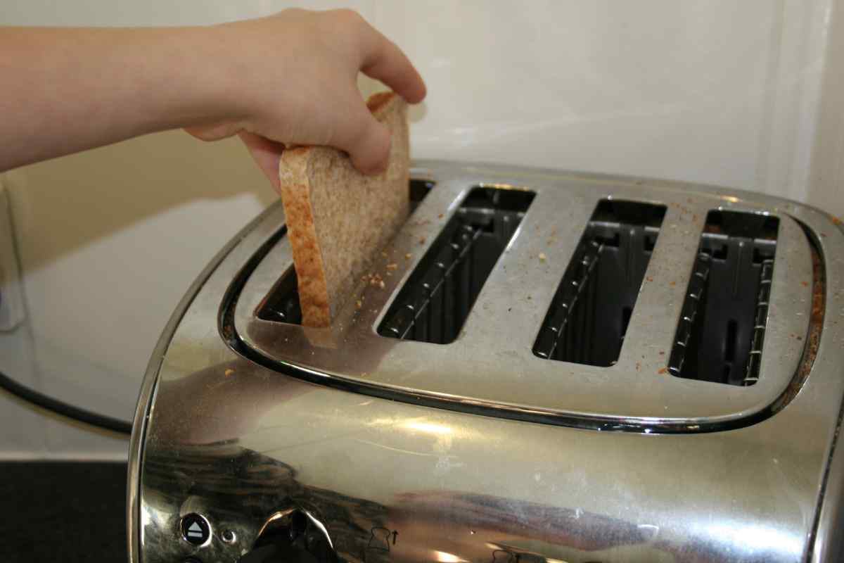 Picture of a child's hand putting bread into a toaster, as part of a blog about a Valentine's recipe for kids to make independently called Love Toast.