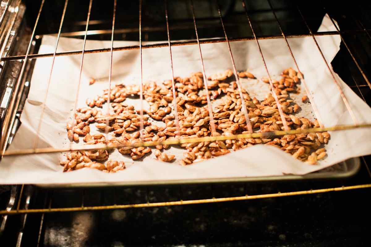 Image of some pumpkin seeds roasting in an oven on a baking tray with parchment paper, as part of a blog about what to do with your pumpkin seeds with kids